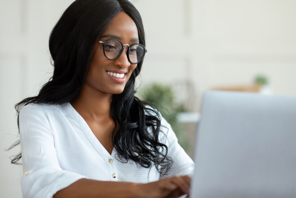 Smiling black woman, wearing a white blouse, working at her computer.