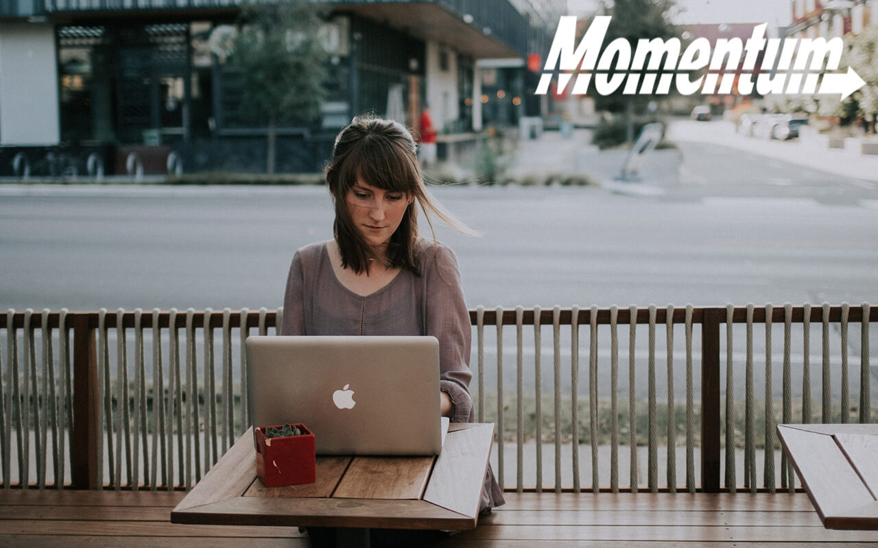 Woman sitting at a table at an outdoor cafe, working on her laptop.